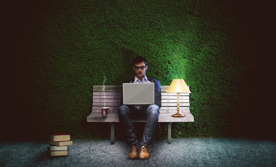 A man sitting on a bench working on a laptop